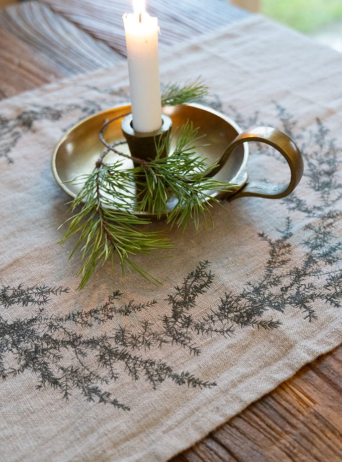 bordslöpare i oblekt linne med tryck av grankvist, liggande på ett bord