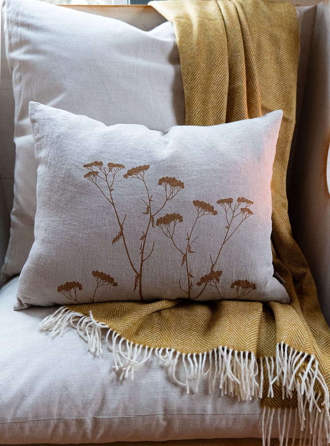 kudde i oblekt linne liggande i en fåtölj med en gul pläd