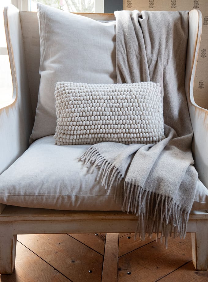 en fåtölj med en plad draperad över ryggen och en kudde i ull i sitsen