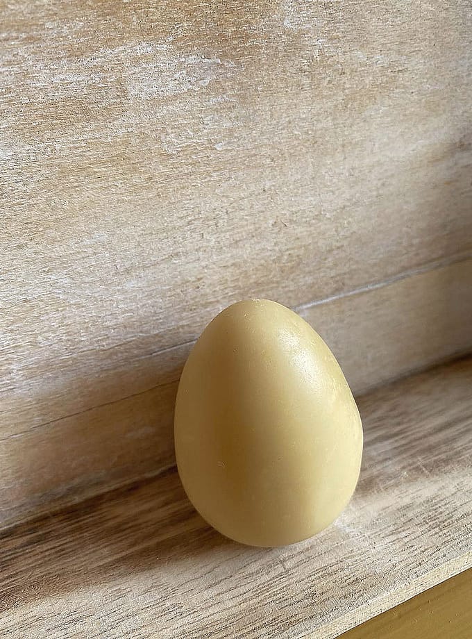 gul, äggformad bixax balm mot en bakgrund i trä