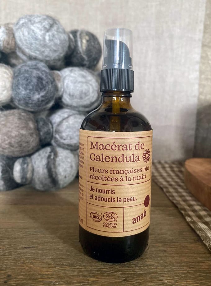 brun glasflaska med calendulaolja och en etikett på franska stående på ett träbord