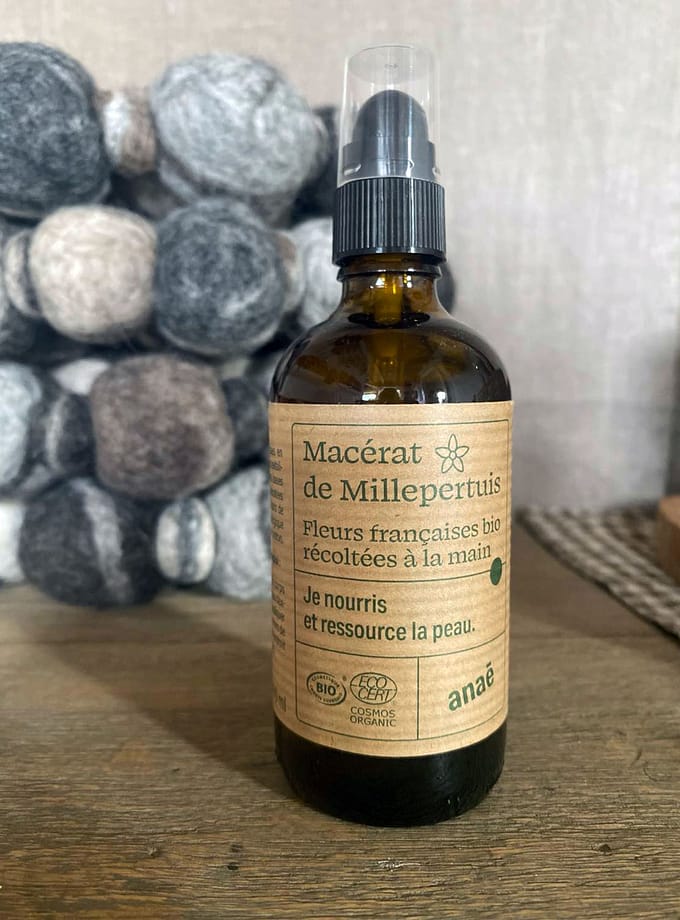 brun glasflaska med johannesörtsolja och en etikett på franska stående på ett träbord