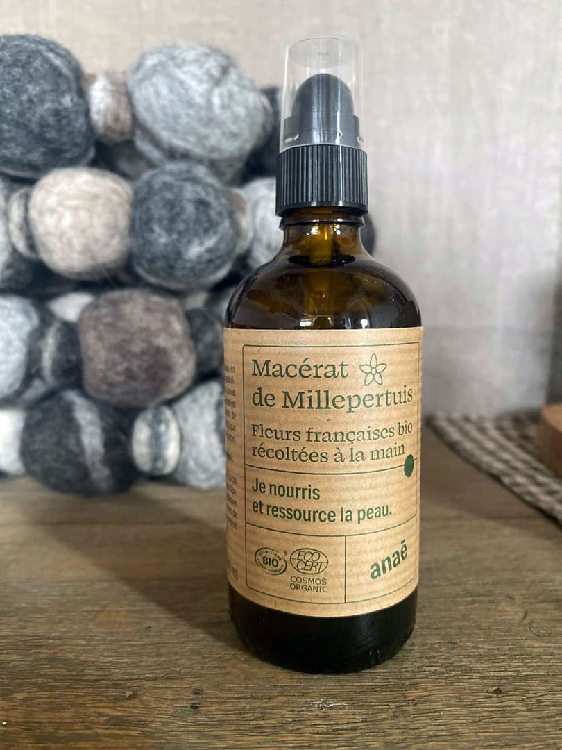 brun glasflaska med johannesörtsolja och en etikett på franska stående på ett träbord